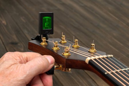 Photo for Hand tuning a guitar with a tuner. Close up. - Royalty Free Image