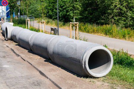 Gray concrete pipes for plumbing and drainage lying on the edge of a construction site.