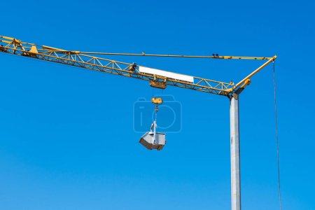 Photo for A metal container hangs on a hook of a yellow crane against a clear blue sky. - Royalty Free Image