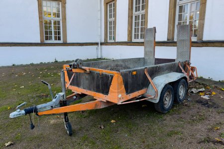 A small car trailer for transporting goods against the background of a building wall.