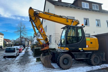 A yellow wheeled excavator standing in front of a residential building.