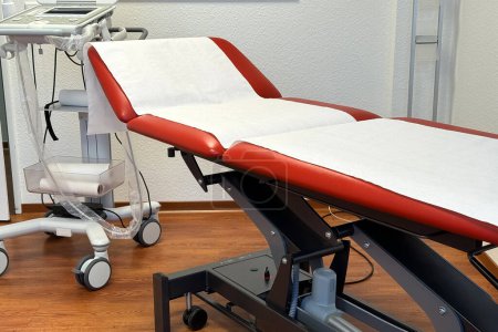 Un lit mobile rouge recouvert d'une serviette en papier dans un cabinet de médecin. Gros plan.