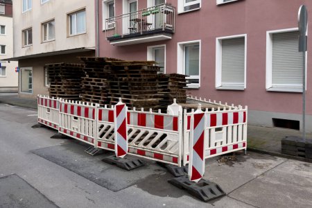 Wooden pallets stacked on the side of the road are fenced with white and red plastic barriers.