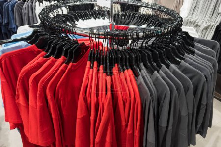 A round hanger in a store on which red and gray T-shirts are hung. Close-up.