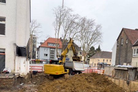 Un pequeño sitio de construcción donde una excavadora amarilla carga tierra en un camión.