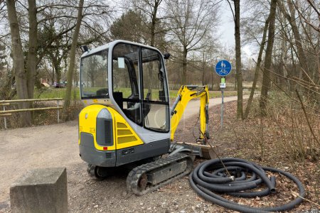 A small yellow crawler tractor in a park in early spring near the pedestrian path.