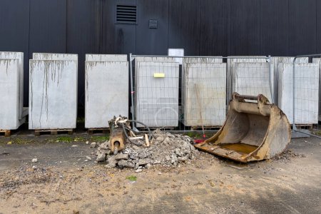 Cubo de excavadora en un sitio de construcción junto a una pila de residuos de construcción. Bloques de hormigón en el fondo.