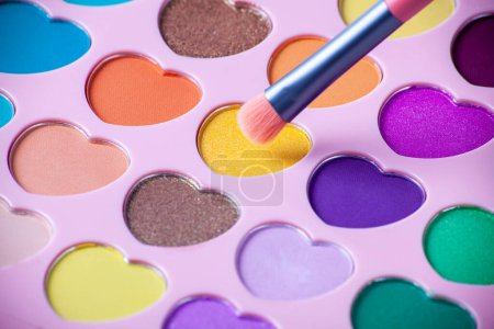 Foto de Palette of eyeshadows with multicolor heart-shaped refilles close up. Eyeshadows in macro. Cosmetic brush - Imagen libre de derechos