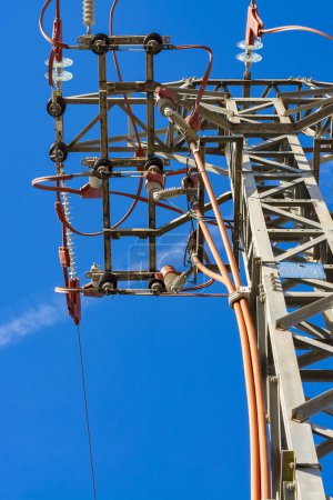 Foto de Parte superior de una torre de línea de energía con cables y detalles rojos, vistos desde abajo, con cielo azul. Imagen vertical - Imagen libre de derechos