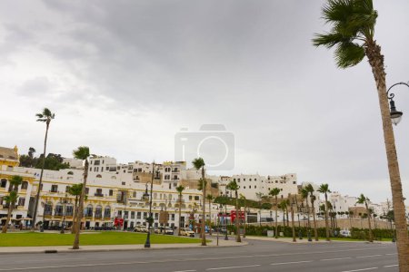 Photo for Tangier, Morocco. October 15th, 2022 - The Spain Square, with palm trees and terraces of restaurants and bars, next to a ramp to a gate of the walled medina - Royalty Free Image