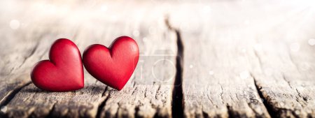 Téléchargez les photos : Deux coeurs en bois sculpté à la main rouge sur la table rustique avec la lumière du soleil et Bokeh - Saint Valentin - en image libre de droit