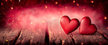 Téléchargez les photos : Deux coeurs en bois sculptés à la main rouge sur une table rustique avec fond Bokeh lumineux - Saint Valentin - en image libre de droit