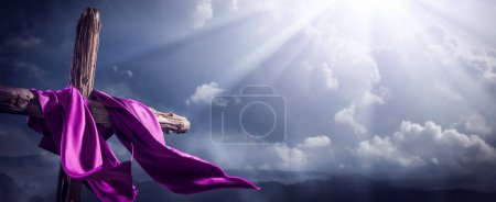 Foto de Fluyendo la túnica púrpura en la cruz de madera con la luz del cielo brillando a través de las nubes - La resurrección y la ascensión de Jesucristo - Imagen libre de derechos