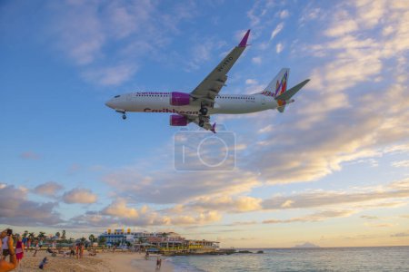 Téléchargez les photos : Caribbean Airlines Boeing 737 Max 8 survolant Maho Beach au coucher du soleil avant d'atterrir sur l'aéroport international Princess Juliana SXM à Sint Maarten, aux Pays-Bas Caraïbes. - en image libre de droit