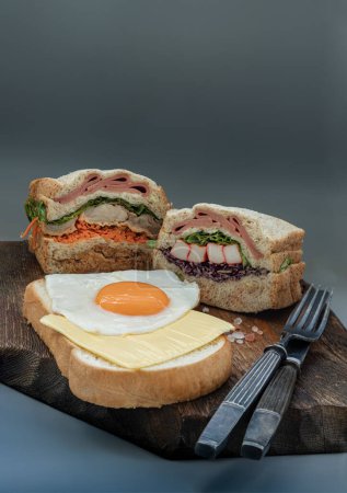 Photo for Homemade Sandwichs stuffed Ham, Cheese, Crab stick and vegetables with Cheese and Fried egg on  Bread served with knife and fork on wooden background. The concept of Healthy delicious food, Space for text, Selective Focus. - Royalty Free Image