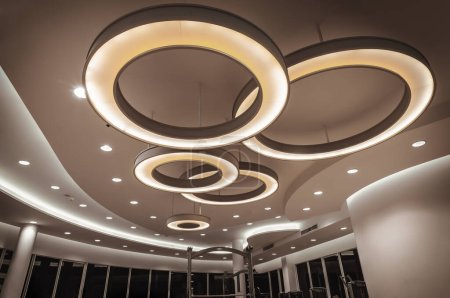 Photo for Hanging rounded ceiling mounted light fixtures with modern LED light bulb. Yellow circular ring shaped lamps hang under ceiling, Architecture and interior design round lights on ceiling. Space for text, Selective focus. - Royalty Free Image
