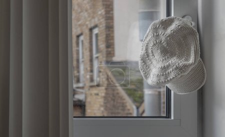 Photo for White cotton crochet hat hung on the glass window handle. Space for text, Selective focus. - Royalty Free Image