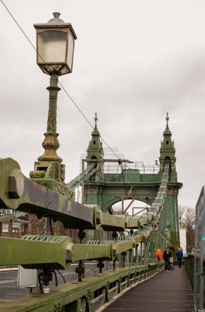 Photo for London, UK - Dec 25, 2023 - Traditional metal Hammersmith bridge for pedestrians and cyclists over the River thames. One of the world's oldest suspension bridges and a major river crossing and primary route in west london, Cast-iron bridge, Space for - Royalty Free Image