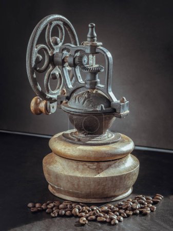 Old original coffee bean original grinder metal shake wheel with hand crank and coffee beans on dark background. Antique coffee grinder with traces of time and scuffs on the body, Copy space, Selective focus.