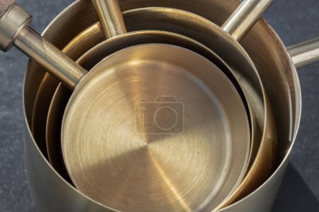 Set of Brass Measuring Cups with Wood Handles with Hanging Hole Design on dark background. Close-up of Wooden & Brass Measuring Cups & Spoons for Measuring Dry and Liquid Ingredients, Kitchen tool, Copy space, Selective Focus.
