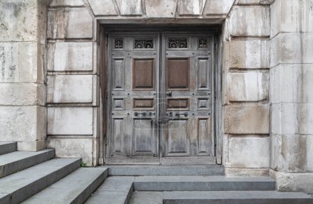 Foto de Londres, Reino Unido - 27 de febrero de 2024 - Cadenas que cierran una entrada antiguas puertas de hierro de madera al lado de una catedral de San Pablo. Puertas de madera encadenadas con escalones de piedra que conducen hacia abajo, Espacio para texto, Enfoque selectivo. - Imagen libre de derechos