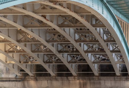 London, UK - 27. Februar 2024 - Detail der Tragkonstruktion und Träger unter der Southwark Bridge über die Themse in London. Die Seite einer türkisfarbenen gusseisernen Brücke, Gebogene Stahlbrücke, Raum für Text, Selektiver Fokus.