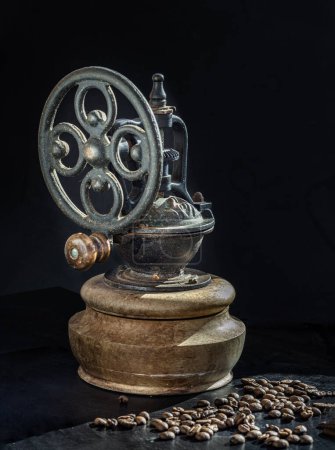 Antique coffee original grinder metal shake wheel with hand crank and coffee beans on dark background. Old original coffee grinder with traces of time and scuffs on the body, Space for text, Selective focus.