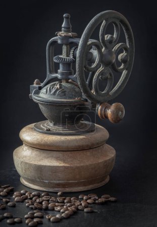 Antique coffee bean original grinder metal shake wheel with hand crank and coffee beans on dark background. Old original coffee grinder with traces of time and scuffs on the body, Space for text, Selective focus.