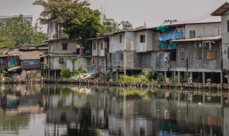 Foto de Bangkok, Tailandia - 20 de abril de 2024 - En la zona de tugurios, las casas son antiguas a lo largo del Khlong Phra Khanong. Casas rotas están al lado del Canal con agua sucia. Problema de mala contaminación, Espacio para texto, Enfoque selectivo. - Imagen libre de derechos