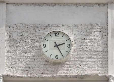 Round white watch face with numbers hanging on white brick wall. Clock dial face in front of brick wall, Space for text, Selective focus.