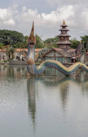 Bangkok, Thailand - 16 Jun, 2023 - Beautiful scenery view of King of Naga statues (Serpent King) in the pond and the Ancient wooden northern thai style house background. Asian Architecture, Space for text, Selective focus.