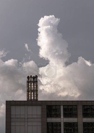Vier Schornsteine auf dem Flachdach eines großen Gebäudes mit flauschig weißen Wolken am Himmel im Hintergrund. Raum für Text, selektiver Fokus.