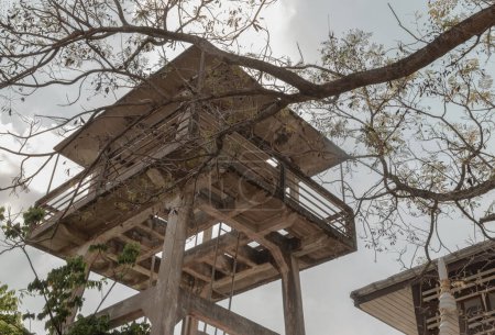 Vista de abajo hacia arriba de las ramas del árbol frente a la antigua torre de agua hecha de cemento y escalera de metal con fondo de cielo. Enfoque selectivo. Enfoque selectivo.