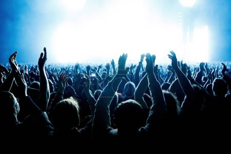 Una multitud de personas con los brazos levantados durante un concierto de música con un espectáculo de luz increíble. Siluetas negras.