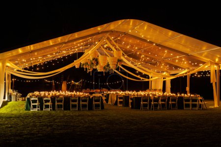 Photo for A large white event tent, decorated with twinkling string lights and a stunning chandelier, provides a romantic and enchanting atmosphere. - Royalty Free Image