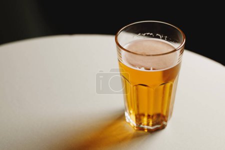 Photo for A refreshing pint of beer on a white table with a dark backdrop. - Royalty Free Image