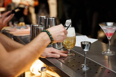 Ein erfahrener Barkeeper gießt Eis in ein Glas mit einem geschüttelten Cocktail