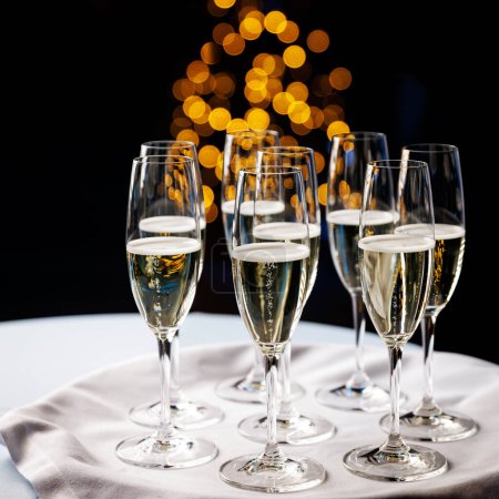 Foto de Un arreglo festivo de flautas de champán llenas de vino espumoso, con un telón de fondo de cálidas luces doradas bokeh. - Imagen libre de derechos
