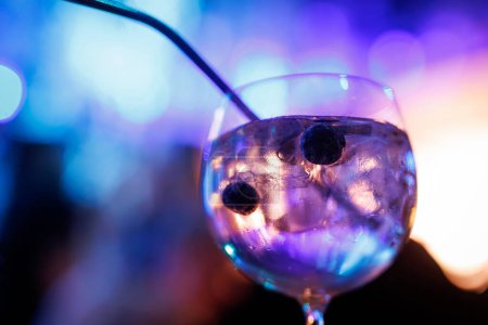 Close-up of Gin and tonic cocktail with blueberries, illuminated by enchanting multicolored lights in the background