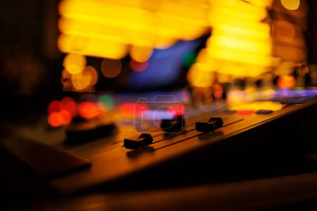 Modern sound mixer console with colorful buttons and sliders, set against the backdrop of a live music venue.