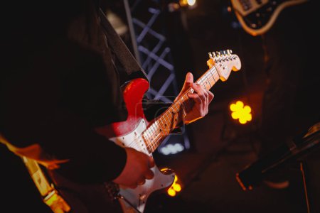 The guitarist plays with the group on the stage