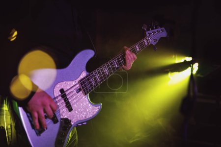 Bass guitarist playing live concert with rock band.