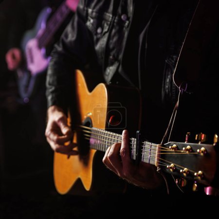 A musician plays a chord on an acoustic guitar during a performance.