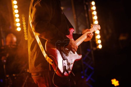 Photo for A passionate musician strums a red electric guitar on stage, illuminated by the warm glow of surrounding lights. - Royalty Free Image