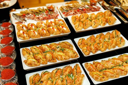A lavish spread of gourmet appetizers, featuring golden croissants garnished with fresh herbs and a variety of delicious fillings