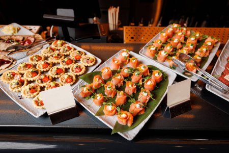 Les rouleaux de saumon sont placés sur des assiettes carrées bordées de feuilles de banane pour une présentation esthétique.