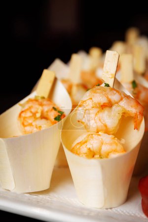 Aperitivos de camarones gourmet servidos elegantemente en conos de madera individuales, capturando la esencia de un sofisticado catering.