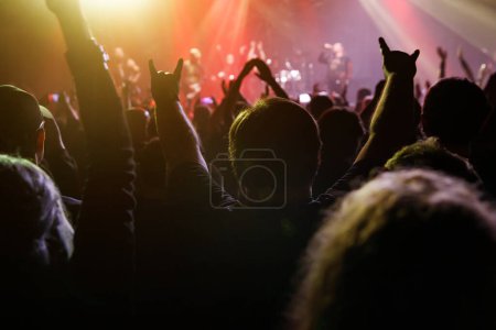 Silhouetten enthusiastischer Fans mit erhobenen Händen werden von den Strahlen der Bühnenlichter beleuchtet