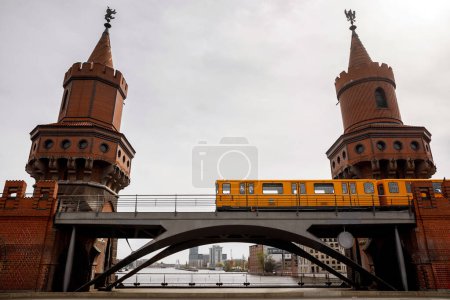 Żółty Berlin wagonów metra poruszających się wzdłuż czerwonej cegły zabytkowego mostu. Wagony między wieżami