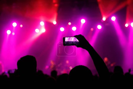 Capturing the electrifying atmosphere of a live music event, an audience member recording or taking a photo with their smartphone.
